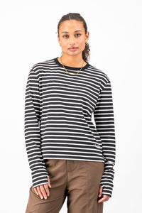 A woman modeling a black and white horizontally striped long-sleeve knit top with a crew neck, paired with brown pants, against a plain white studio background.